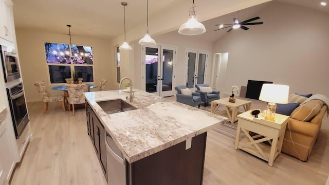 kitchen with a kitchen island with sink, light wood-style flooring, a sink, open floor plan, and stainless steel appliances