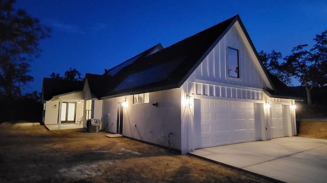 property exterior at night with concrete driveway and a garage