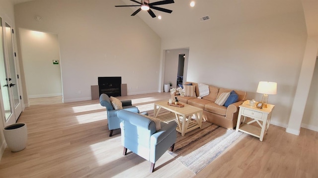 living room featuring ceiling fan, visible vents, high vaulted ceiling, and light wood-style flooring