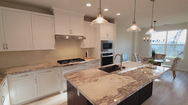 kitchen with under cabinet range hood, a sink, tasteful backsplash, stainless steel appliances, and light stone countertops