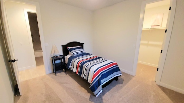 bedroom featuring a walk in closet, baseboards, and light colored carpet