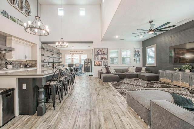 living room featuring ceiling fan with notable chandelier, a high ceiling, visible vents, and light wood-style flooring