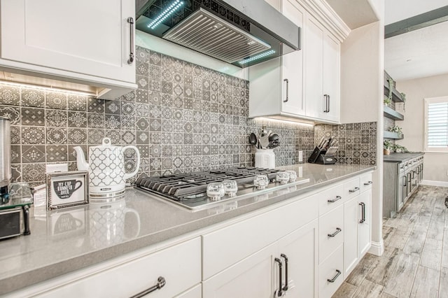 kitchen featuring stainless steel gas cooktop, backsplash, white cabinetry, light wood-type flooring, and premium range hood