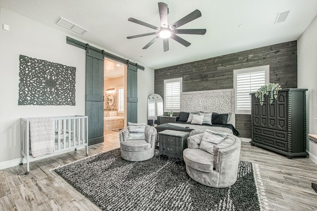 bedroom with a barn door, an accent wall, visible vents, and wood finished floors