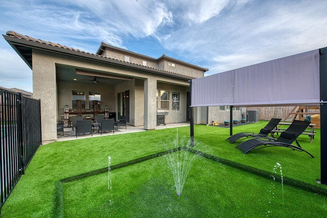 rear view of property with ceiling fan, fence, a yard, stucco siding, and a patio area