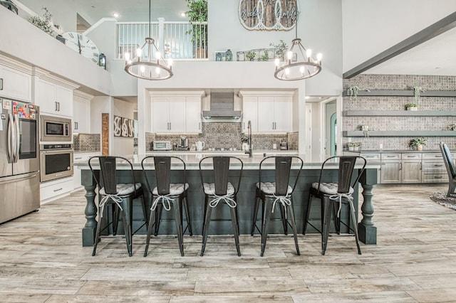 kitchen with a kitchen breakfast bar, stainless steel appliances, wall chimney range hood, and an inviting chandelier