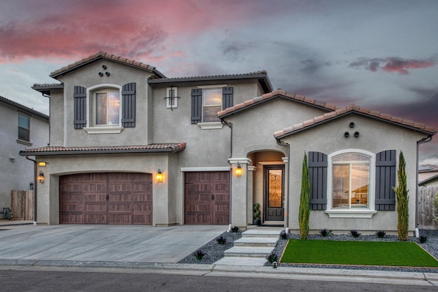 mediterranean / spanish-style home featuring driveway, an attached garage, a tile roof, and stucco siding