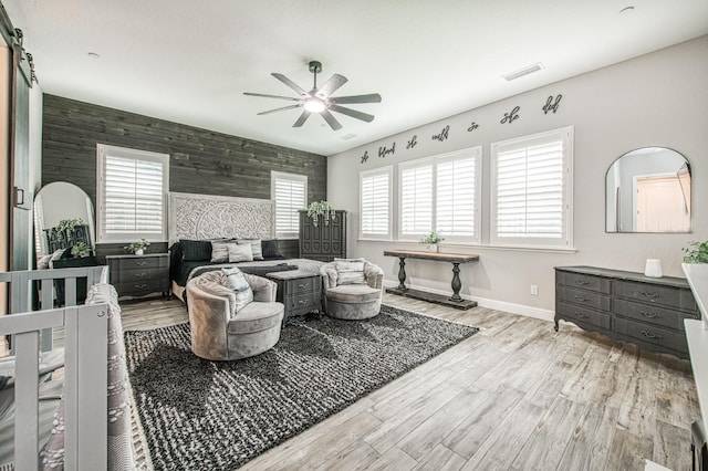 living area featuring an accent wall, wood finished floors, ceiling fan, and a barn door