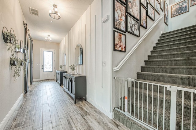 interior space with visible vents, baseboards, stairs, light wood finished floors, and an inviting chandelier