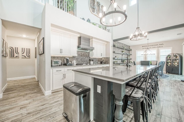 kitchen featuring light wood finished floors, tasteful backsplash, wall chimney exhaust hood, an inviting chandelier, and a sink