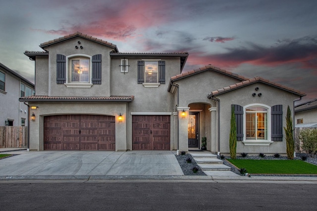 mediterranean / spanish-style home with a tiled roof, an attached garage, driveway, and stucco siding