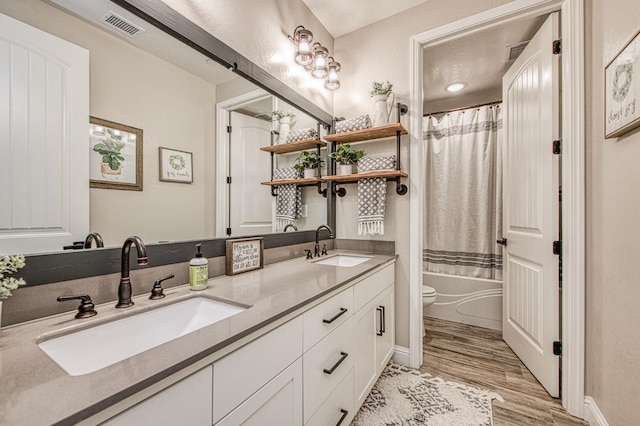 full bath with toilet, wood finished floors, a sink, visible vents, and double vanity