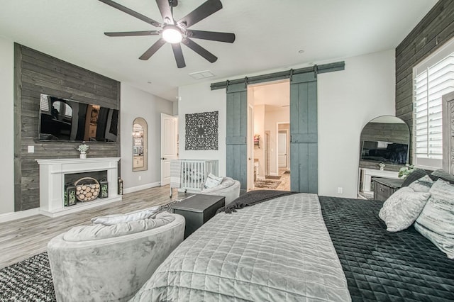 bedroom with a barn door, a fireplace, baseboards, and wood finished floors