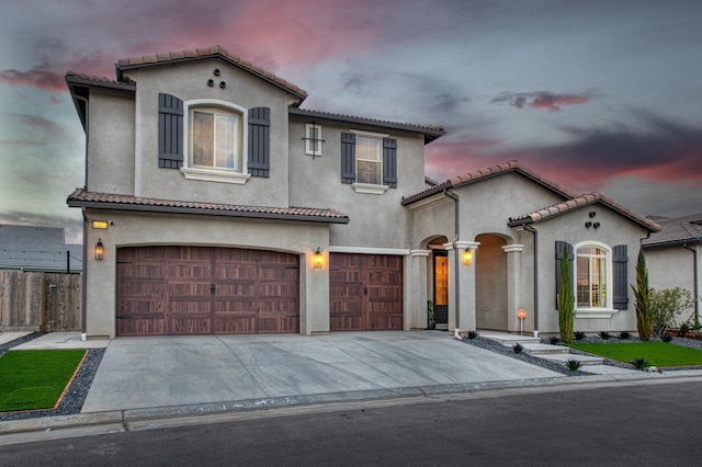 mediterranean / spanish house with an attached garage, a tiled roof, concrete driveway, and stucco siding