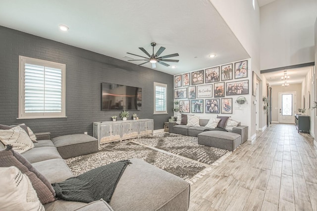 living area featuring ceiling fan, an accent wall, brick wall, wood finished floors, and baseboards