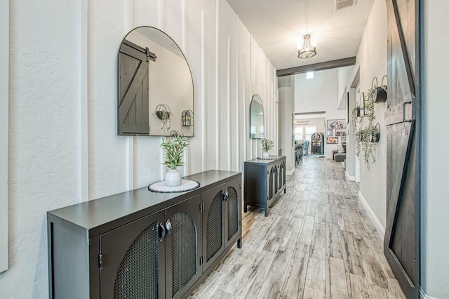 corridor with light wood-style floors, visible vents, baseboards, and a textured wall