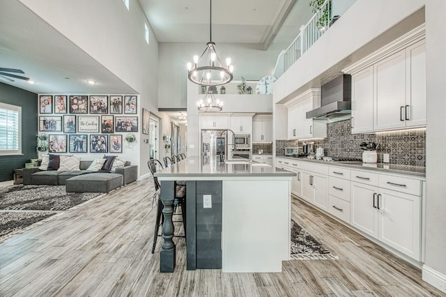 kitchen featuring appliances with stainless steel finishes, light wood-type flooring, backsplash, and wall chimney range hood