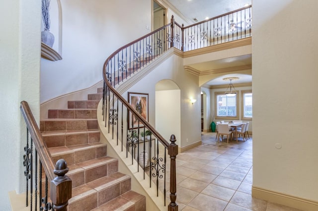 staircase with arched walkways, a high ceiling, ornamental molding, baseboards, and tile patterned floors