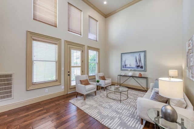 living area featuring ornamental molding, wood-type flooring, a towering ceiling, and baseboards