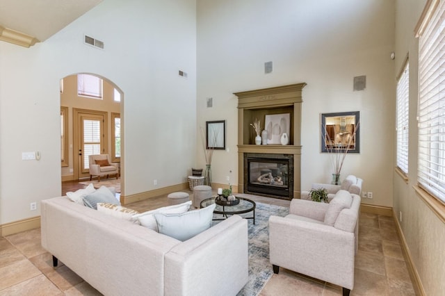 living area with arched walkways, visible vents, a glass covered fireplace, and a towering ceiling