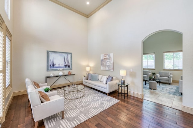 living room with baseboards, arched walkways, a towering ceiling, hardwood / wood-style flooring, and crown molding