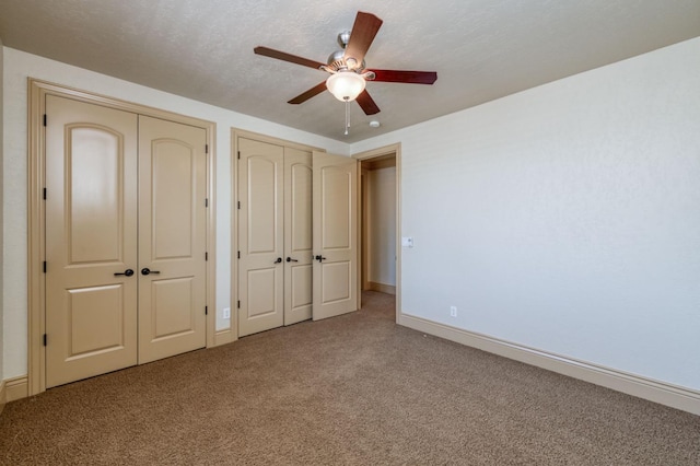 unfurnished bedroom featuring a textured ceiling, ceiling fan, carpet flooring, baseboards, and two closets