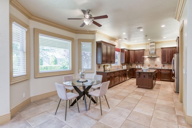 kitchen with crown molding, backsplash, freestanding refrigerator, a kitchen island, and wall chimney range hood