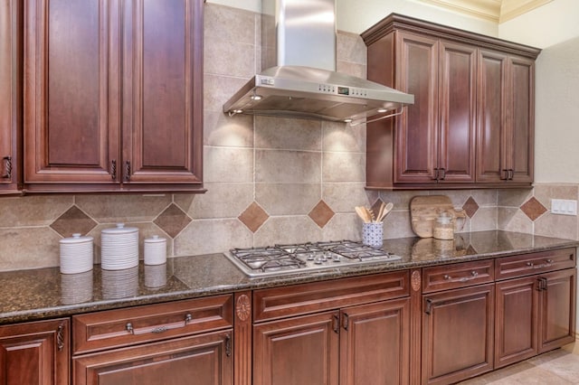 kitchen featuring tasteful backsplash, wall chimney exhaust hood, stainless steel gas cooktop, and dark stone counters