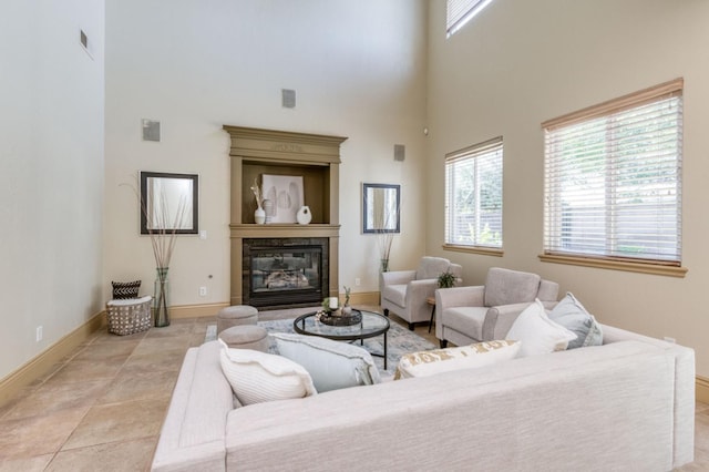 living room with a towering ceiling, light tile patterned floors, baseboards, and a glass covered fireplace