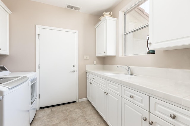 washroom with light tile patterned floors, visible vents, cabinet space, a sink, and separate washer and dryer