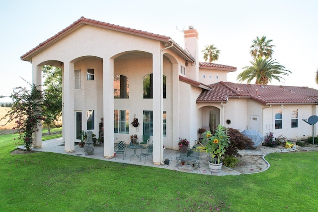 rear view of property featuring a tile roof, a lawn, stucco siding, a chimney, and a patio area