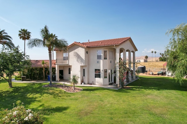 rear view of property with a lawn, a balcony, a tiled roof, a patio area, and stucco siding