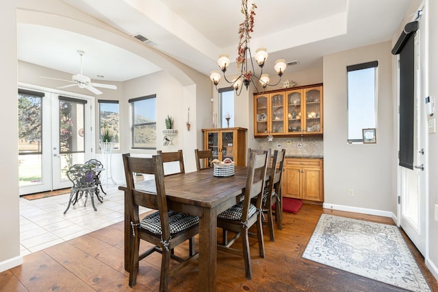 dining space with a tray ceiling, arched walkways, visible vents, wood finished floors, and baseboards