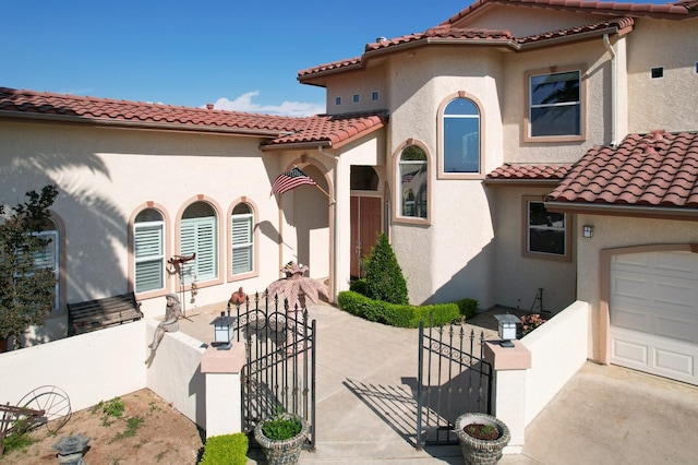 mediterranean / spanish house with a tile roof, a gate, fence, and stucco siding