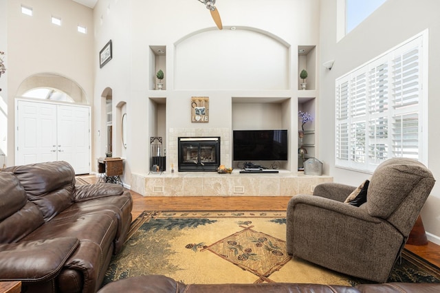 living room with a towering ceiling, built in features, a wealth of natural light, and wood finished floors