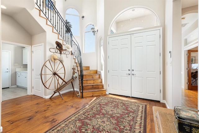 foyer with stairway, baseboards, light wood-style flooring, and a high ceiling