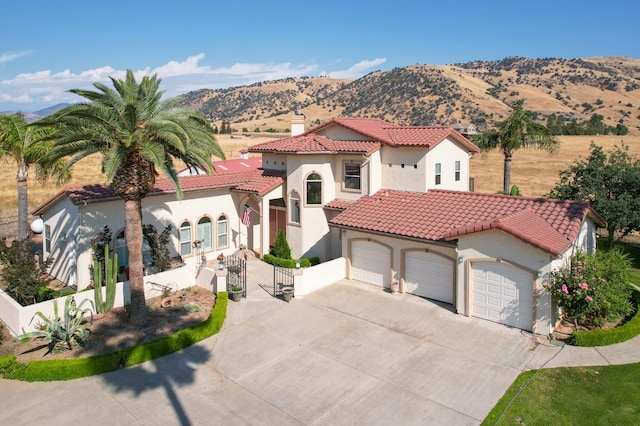 mediterranean / spanish home with fence, a mountain view, a tiled roof, and stucco siding