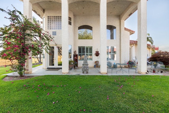 rear view of house featuring french doors, a lawn, and stucco siding