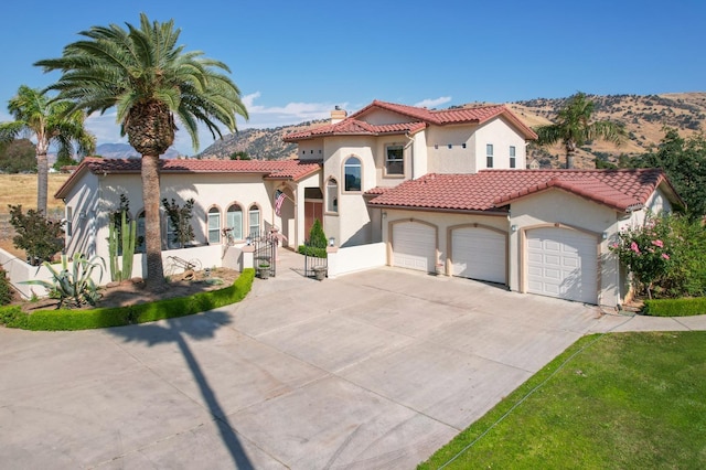 mediterranean / spanish home featuring driveway, a tile roof, a chimney, an attached garage, and stucco siding