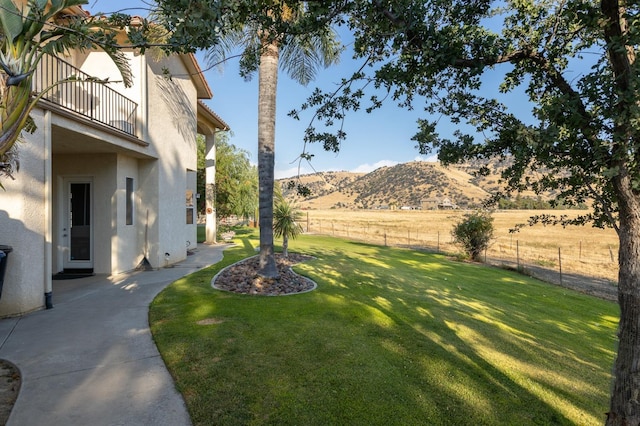 view of yard featuring a balcony, fence, a mountain view, and a rural view