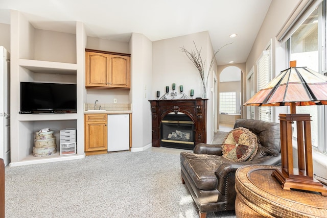 living area featuring light carpet, arched walkways, a glass covered fireplace, and recessed lighting