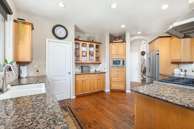 kitchen featuring appliances with stainless steel finishes, arched walkways, a sink, and dark stone counters