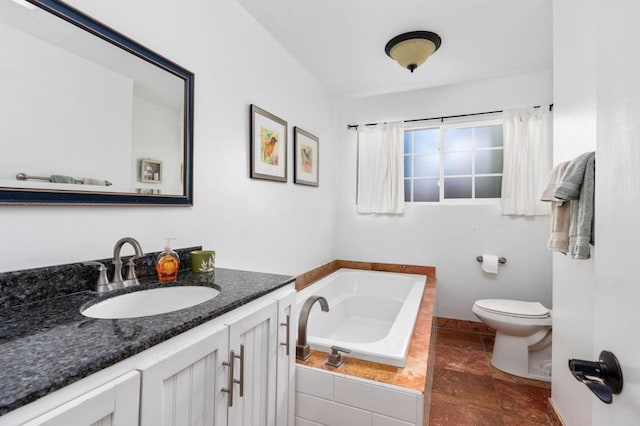 bathroom featuring a garden tub, toilet, vanity, baseboards, and stone finish flooring