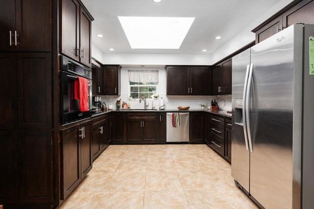 kitchen with a skylight, stainless steel appliances, dark countertops, backsplash, and a sink