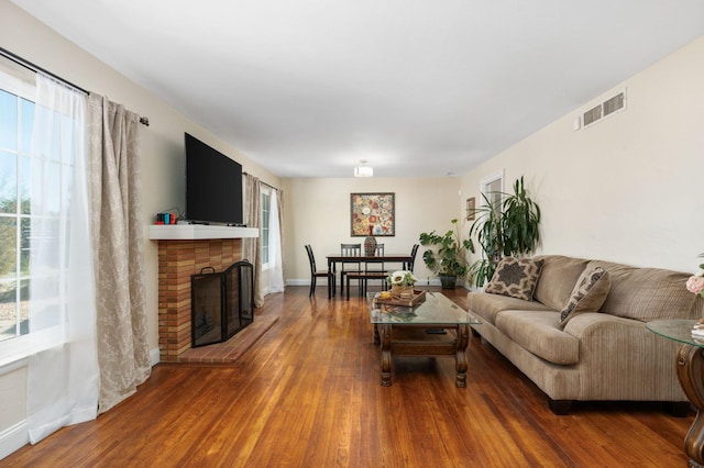 living room featuring a healthy amount of sunlight, a brick fireplace, visible vents, and wood finished floors