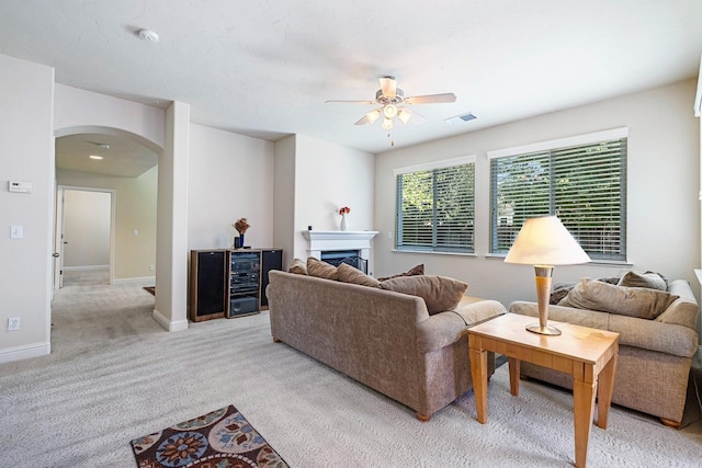 living room featuring light carpet, baseboards, arched walkways, a ceiling fan, and a fireplace