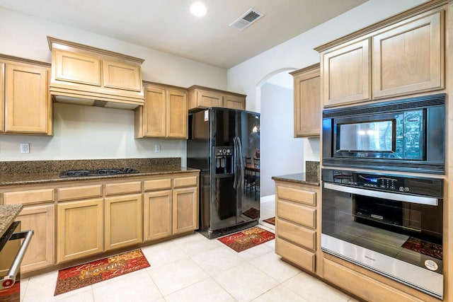 kitchen featuring arched walkways, light tile patterned floors, visible vents, black appliances, and dark stone countertops