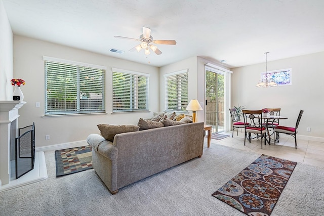 living area with a fireplace, visible vents, light tile patterned flooring, baseboards, and ceiling fan with notable chandelier