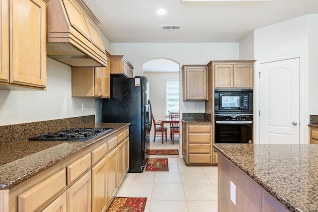 kitchen with visible vents, arched walkways, dark stone countertops, black appliances, and premium range hood