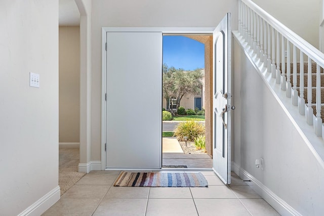 tiled foyer with stairs, baseboards, and arched walkways